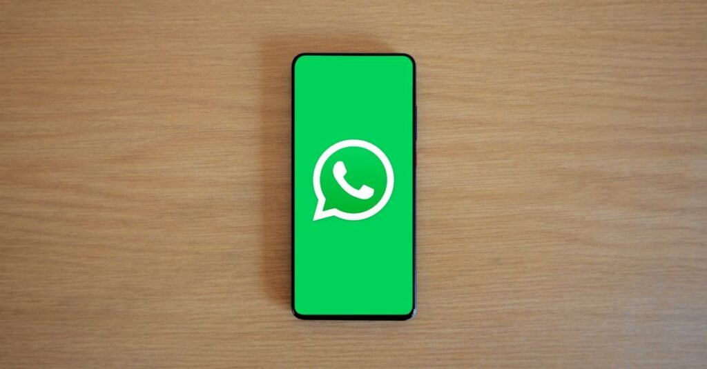 Top view of smartphone displaying WhatsApp logo on a wooden background, representing technology and communication.