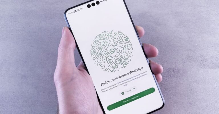 Tampilan dekat tangan yang memegang telepon pintar menampilkan layar selamat datang WhatsApp dalam bahasa Rusia.