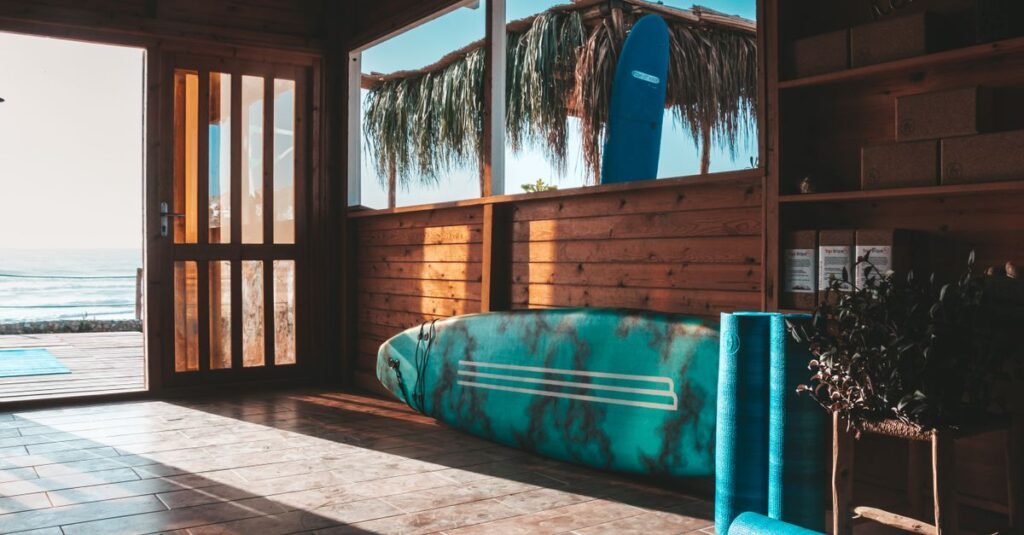 Wooden surf shack interior with surfboard and yoga mat overlooking the ocean at sunrise in Taghazout, Morocco.
