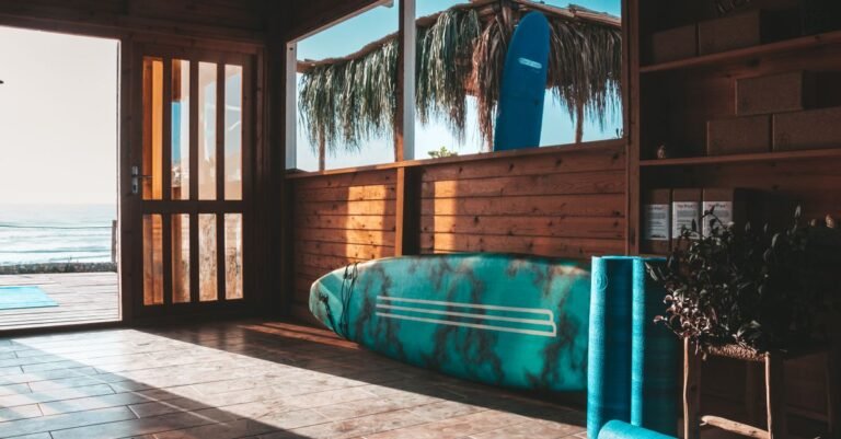 Wooden surf shack interior with surfboard and yoga mat overlooking the ocean at sunrise in Taghazout, Morocco.