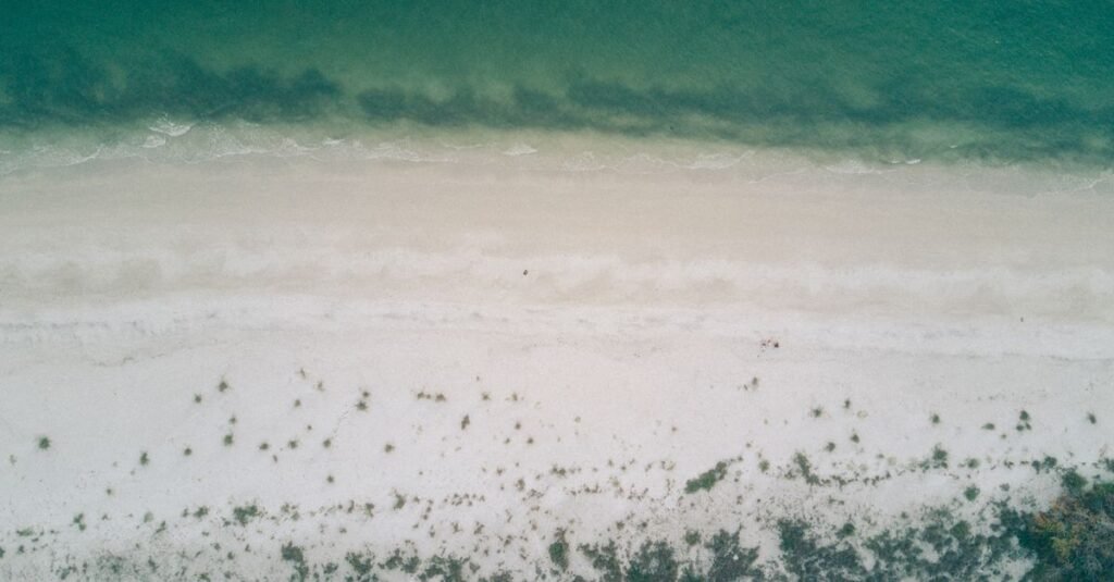 A tranquil aerial view of a serene beach with clear water and soft sand.