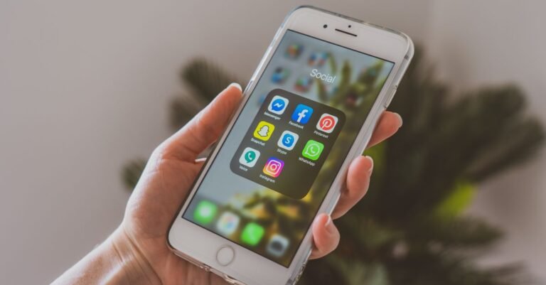 Close-up of a hand holding a smartphone displaying popular social media apps.