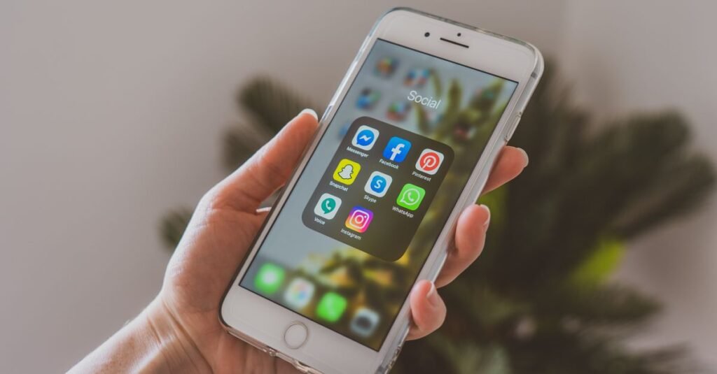 Close-up of a hand holding a smartphone displaying popular social media apps.