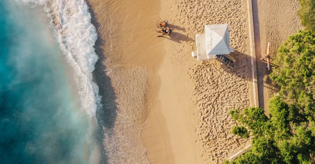 Foto udara yang menakjubkan dari pantai Hawaii dengan gelombang yang cerah dan pemandangan pasir yang tenang saat matahari terbenam.