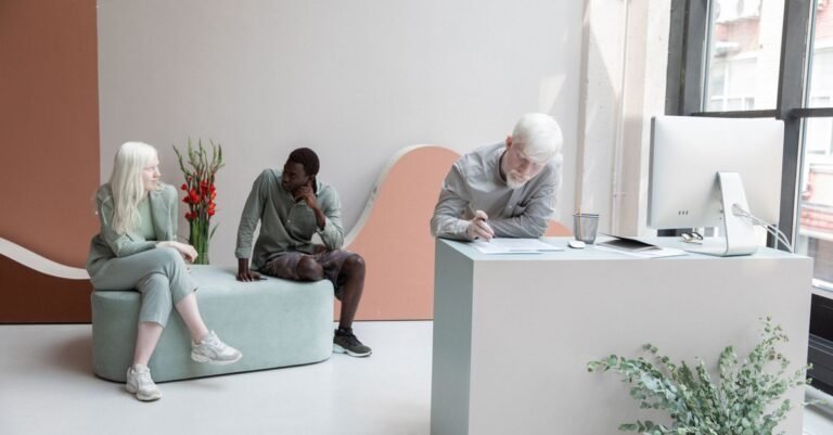Full body of multiethnic coworkers sitting on sofa and writing on paper while working together in contemporary office with computer