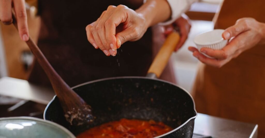 Close-up of hands seasoning a dish in a pot, creating a homemade culinary masterpiece.