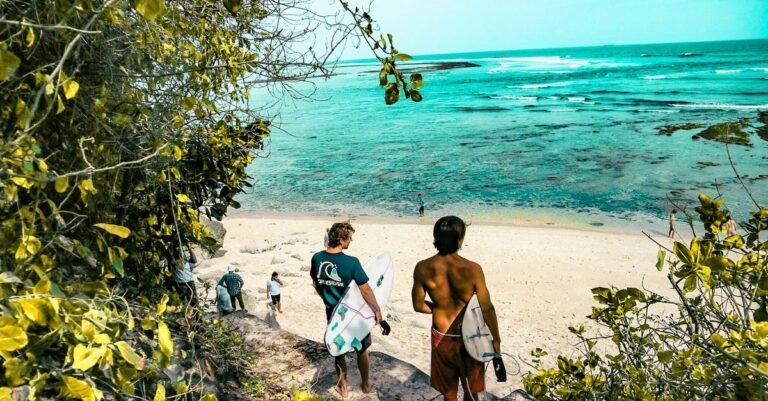 Surfers make their way down a lush path to a stunning beach in Bali, Indonesia.