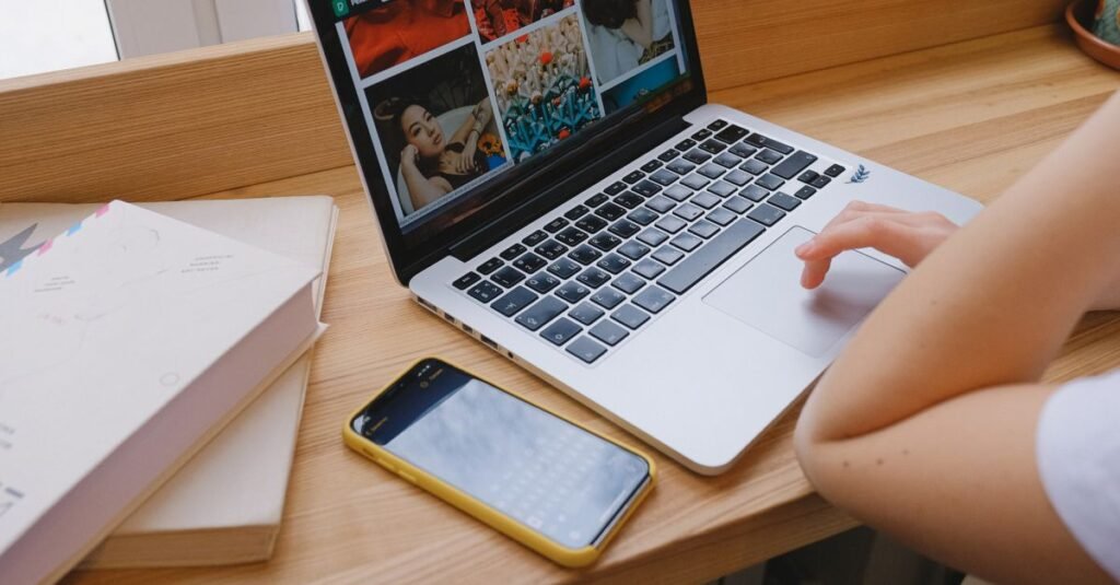 A person using a laptop at a wooden desk with a phone and notebooks nearby, ideal for remote work themes.