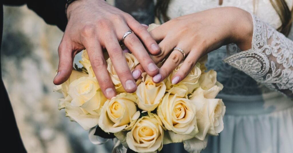Close-up of a couple's hands displaying wedding rings above a bouquet of yellow roses.